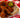 Top-down image of spicy fried chicken piled up on top of white bread and topped with pickle slices, served on a white plate on a red and white checkered tablecloth.