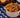 A small bowl of hamburger helper, with Cellentani pasta noodles and Halal ground beef coated in a cheesy tomato sauce and topped with parsley. Served in front of a wooden bowl of garlic bread in the background.