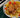 Top down image of golden brown and seasoned Halal chicken thigh resting on top of golden and tender potato slices and chunks of red bell pepper. Served on a gray plate on a dark green striped tablecloth.