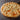 A pizza with chunks of diced chicken and cheese there some visible specs of seasoning. It is on a round wooden board. 