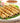 Halal Malai Chicken Kababs sit on a bed of lettuce on a white plate there is rings of red onion behind the kababs and a bowl of brown sauce in the background