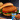 A Halal chicken patty on a bun with tomato and lettuce on a black cutting board. A package of Midamar Chicken Breast Patties is overlaid in the bottom right corner.